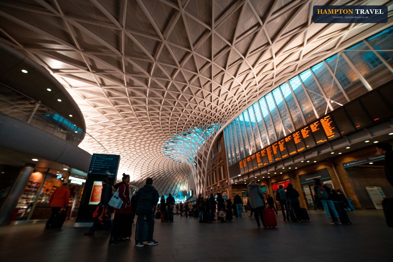 Busy scene inside King's Cross Station with travelers and luggage under iconic roof.